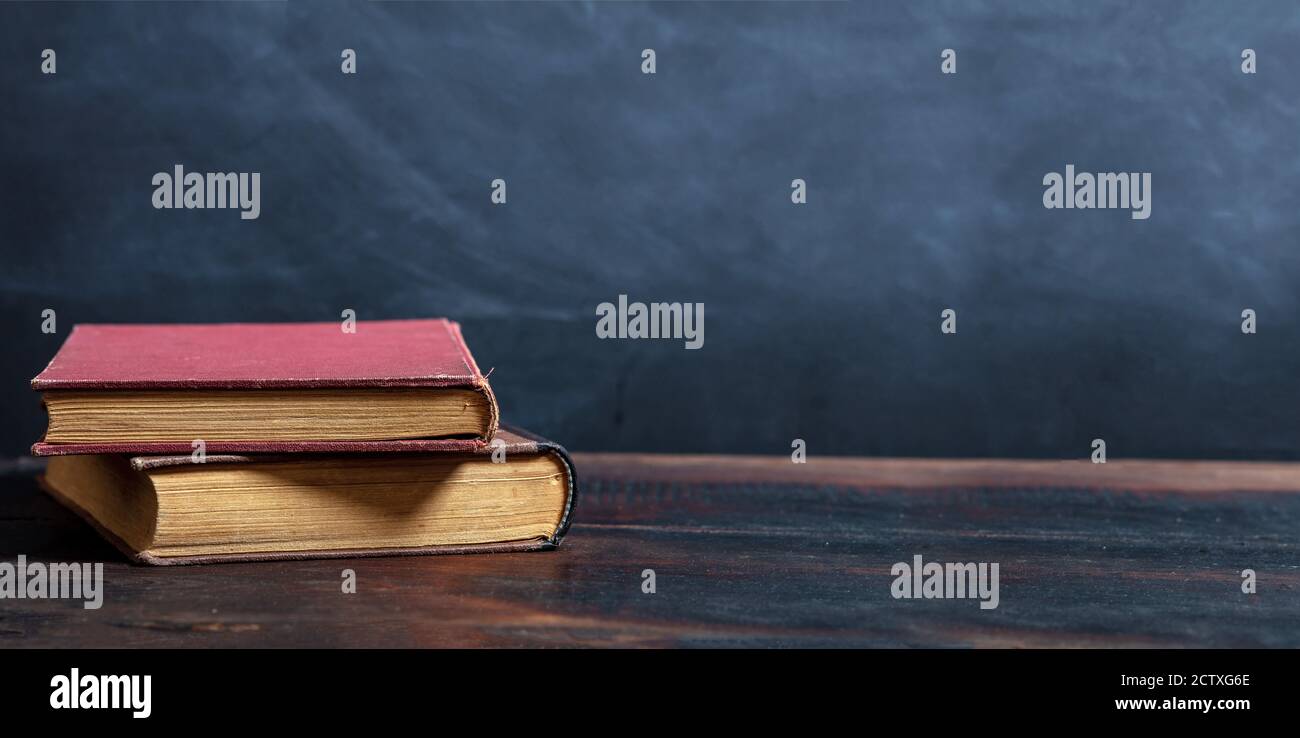 Vecchi libri impilano su un tavolo di legno, sfondo nero del bordo. Biblioteca vintage scrivania di lettura, modello Foto Stock