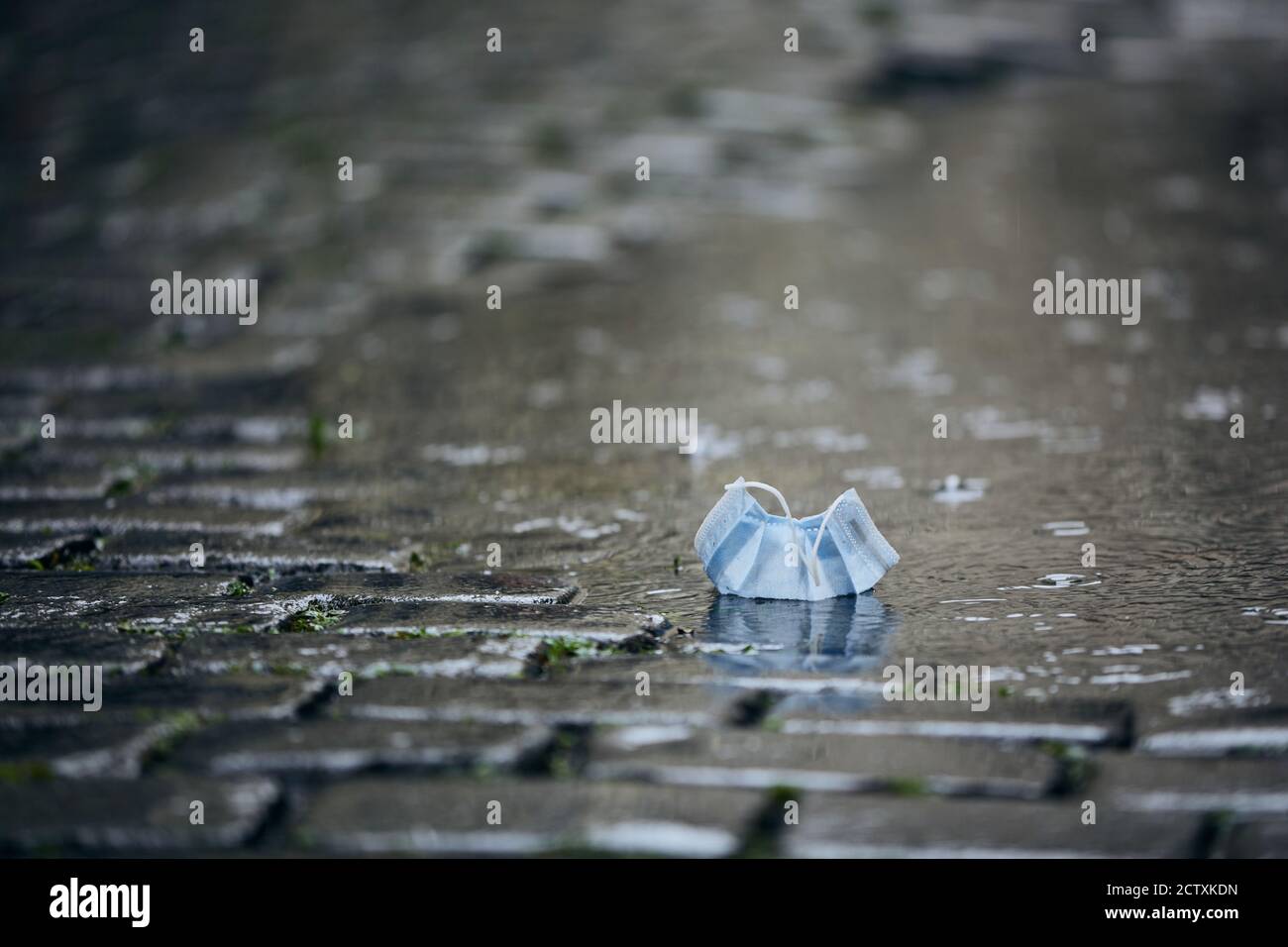 Maschera usa e getta in puddle durante la pioggia. Temi problemi di coronavirus e la vita in nuova normalità. Foto Stock