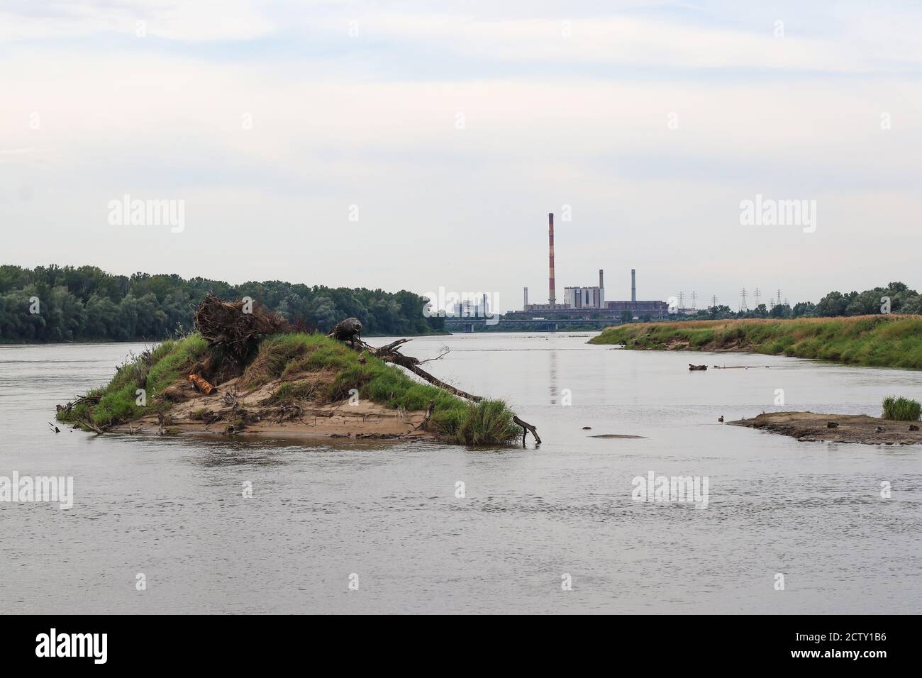 Vista lungo l'ampio fiume con piccola isola in primo piano e. enorme centrale di calore ed energia sullo sfondo Foto Stock