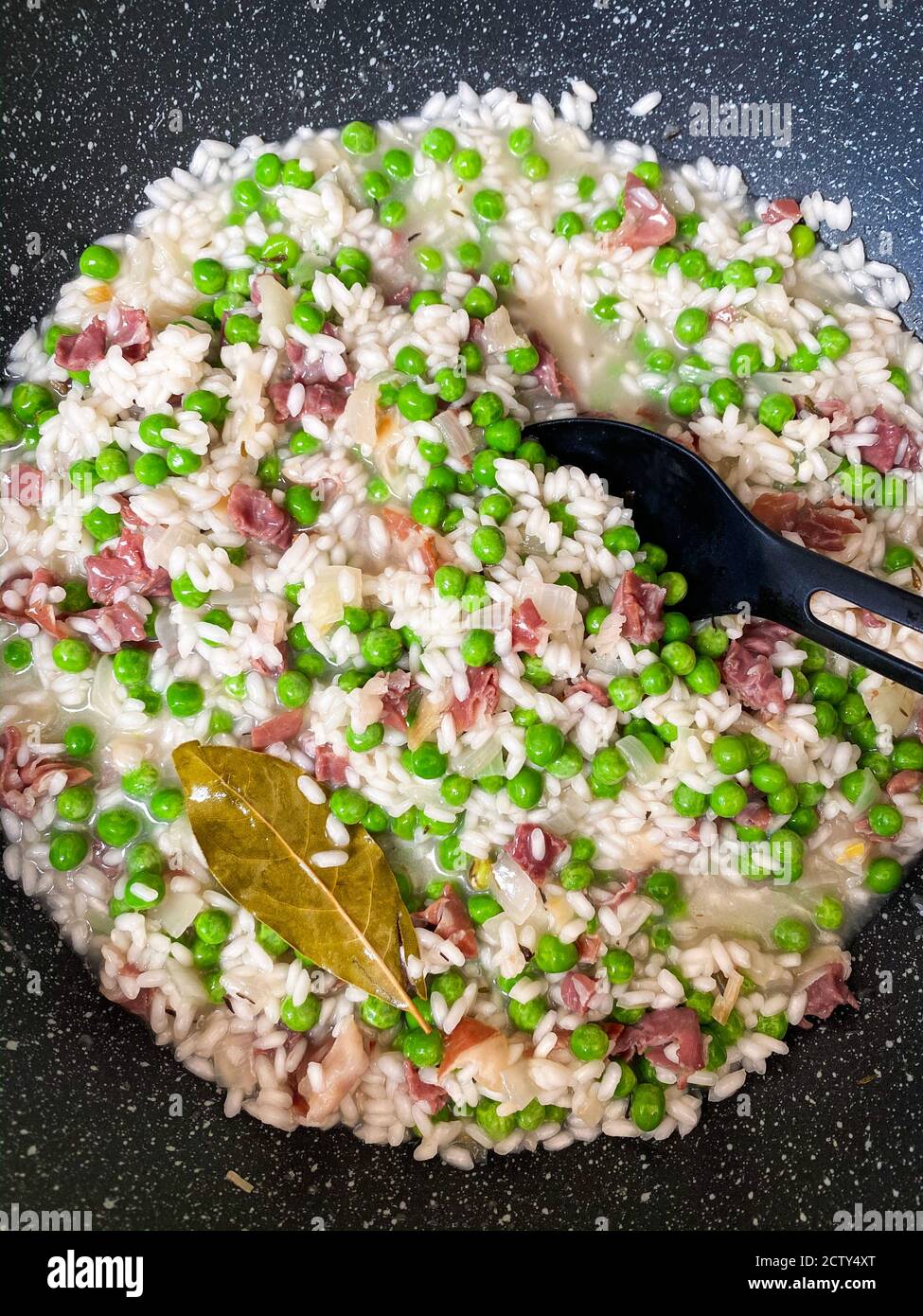 Primo piano - cottura in padella nera di risotti cremosi con piselli, cipolla e prosciutto Foto Stock