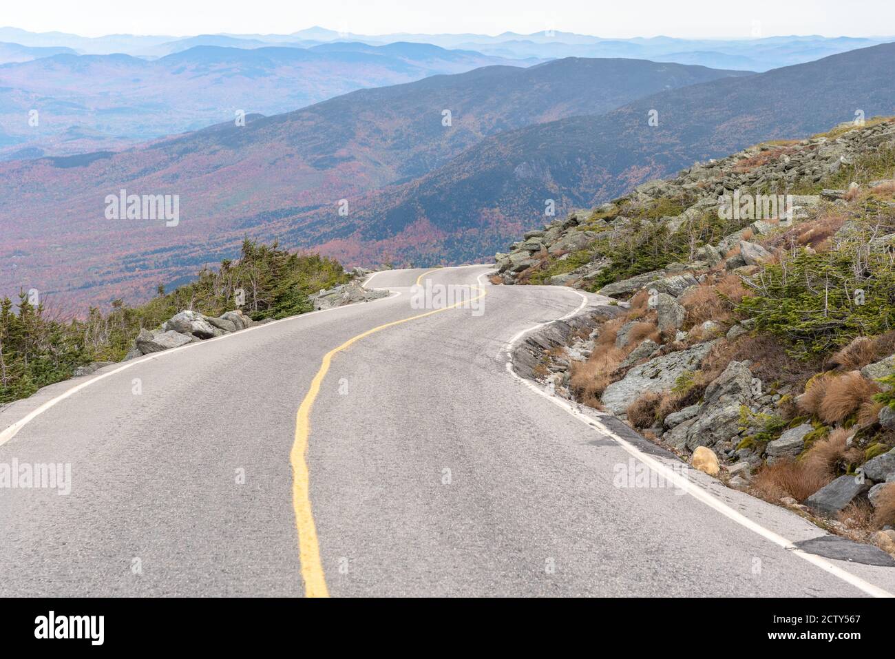 Vuota ripida strada di montagna su una nuvolosa mattina d'autunno. Le montagne boscose sono visibili sullo sfondo. Foto Stock