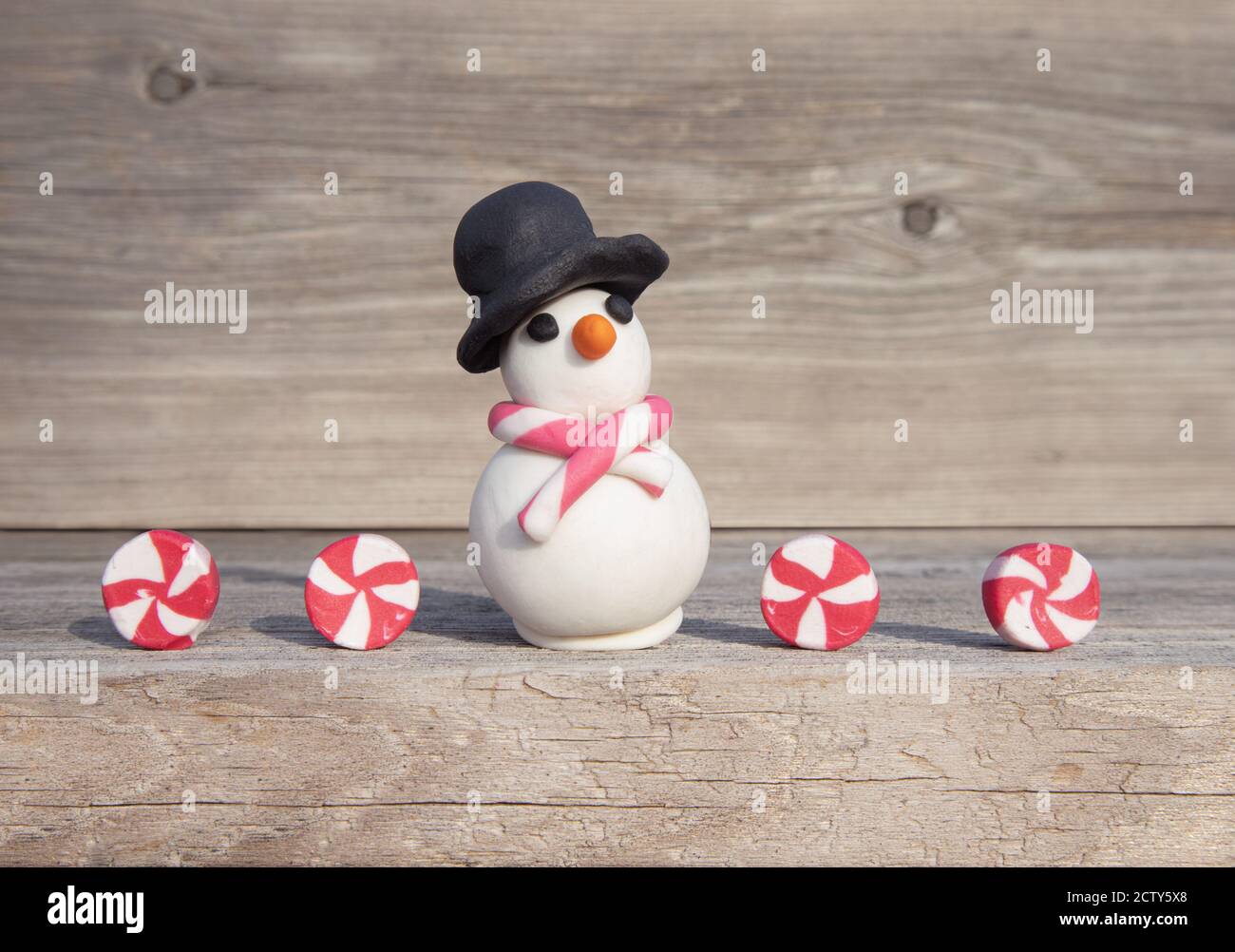 Divertente concetto di Natale. Pupazzo di neve in miniatura con caramelle di fronte a legno morbido sfondo. Realizzato a mano con argilla. Foto Stock