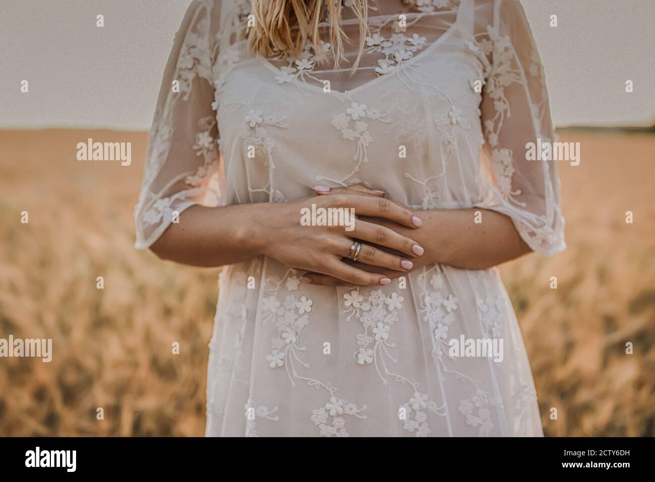 Una donna in un abito da sposa bianco con un la stampa floreale si trova nel mezzo del grano Foto Stock