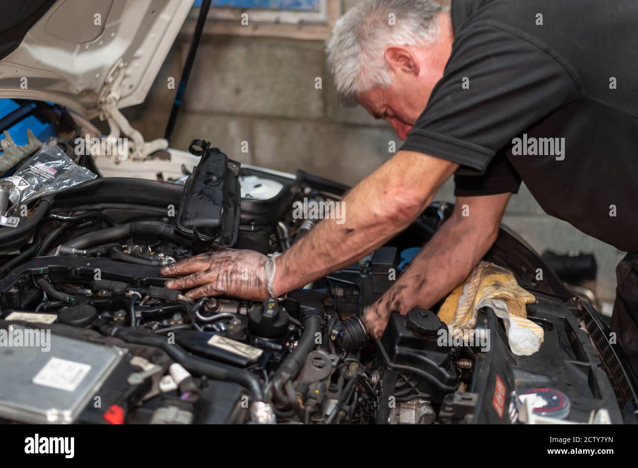 Meccanico senior che lavora sul vano motore per riparare una perdita di olio nel garage di casa. Foto Stock