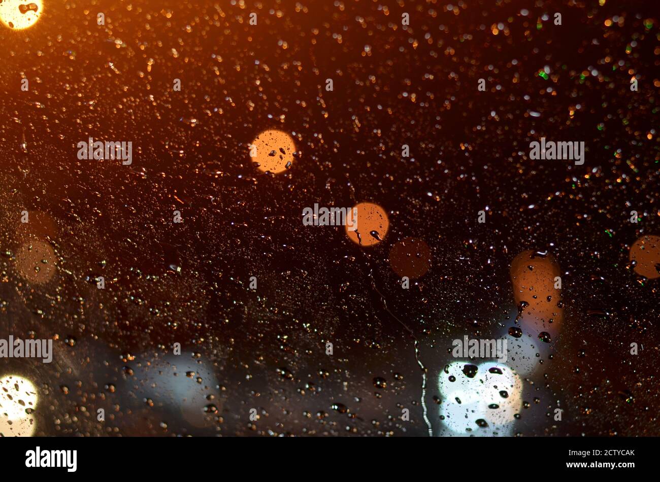 Gocce di pioggia sul vetro della macchina illuminata da lampioni di strada di notte. Foto Stock
