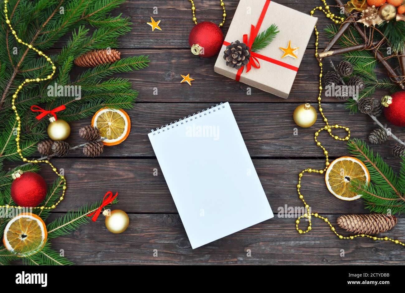 Composizione di Natale o Capodanno con blocco note, decorazioni natalizie, scatola regalo, rami di abete e coni su sfondo di legno vintage con spazio di copia. Foto Stock