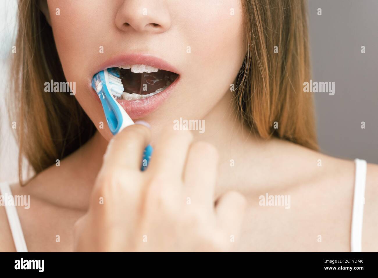 Una giovane donna sta spazzolando i denti in bagno. Riflessione nello specchio Foto Stock