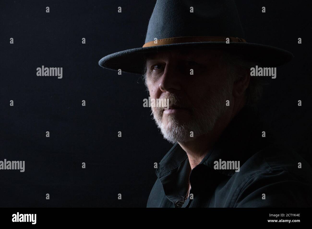 Ritratto in primo piano di un uomo di mezza età in un cappello occidentale largo-brimmed su uno sfondo scuro Foto Stock