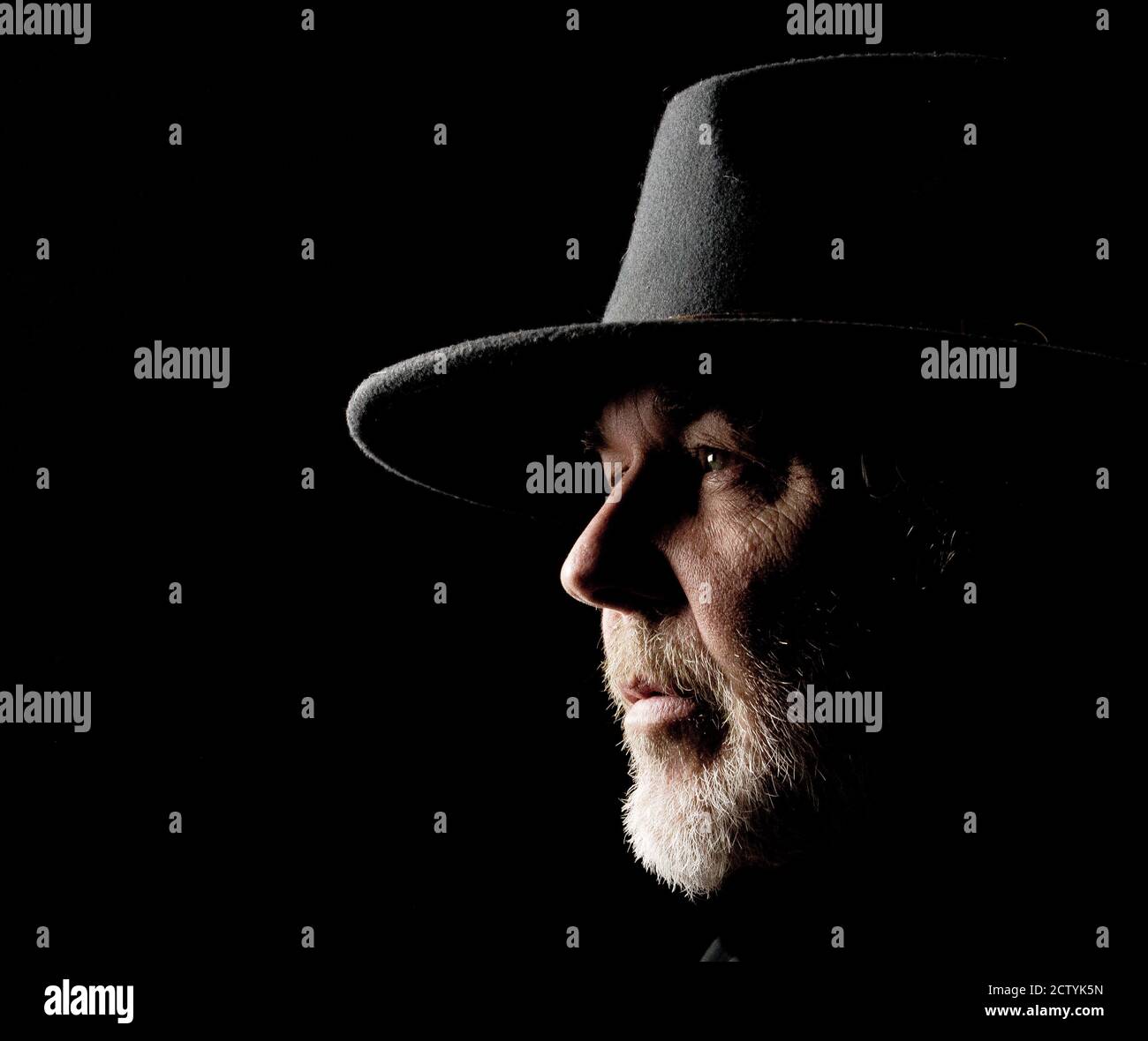 Ritratto in primo piano di un uomo di mezza età in un cappello occidentale largo-brimmed su uno sfondo scuro Foto Stock