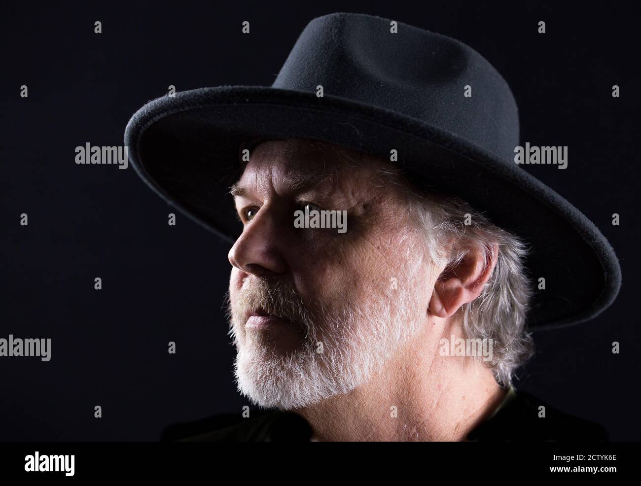 Ritratto in primo piano di un uomo di mezza età in un cappello occidentale largo-brimmed su uno sfondo scuro Foto Stock