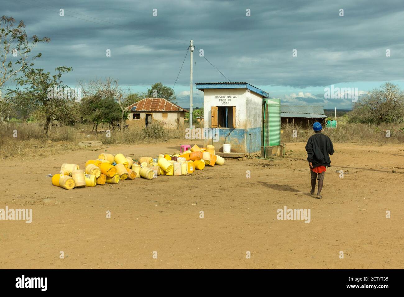 Un uomo africano cammina attraverso contenitori vuoti fuori da un'acqua Chiosco in Kenya rurale Foto Stock