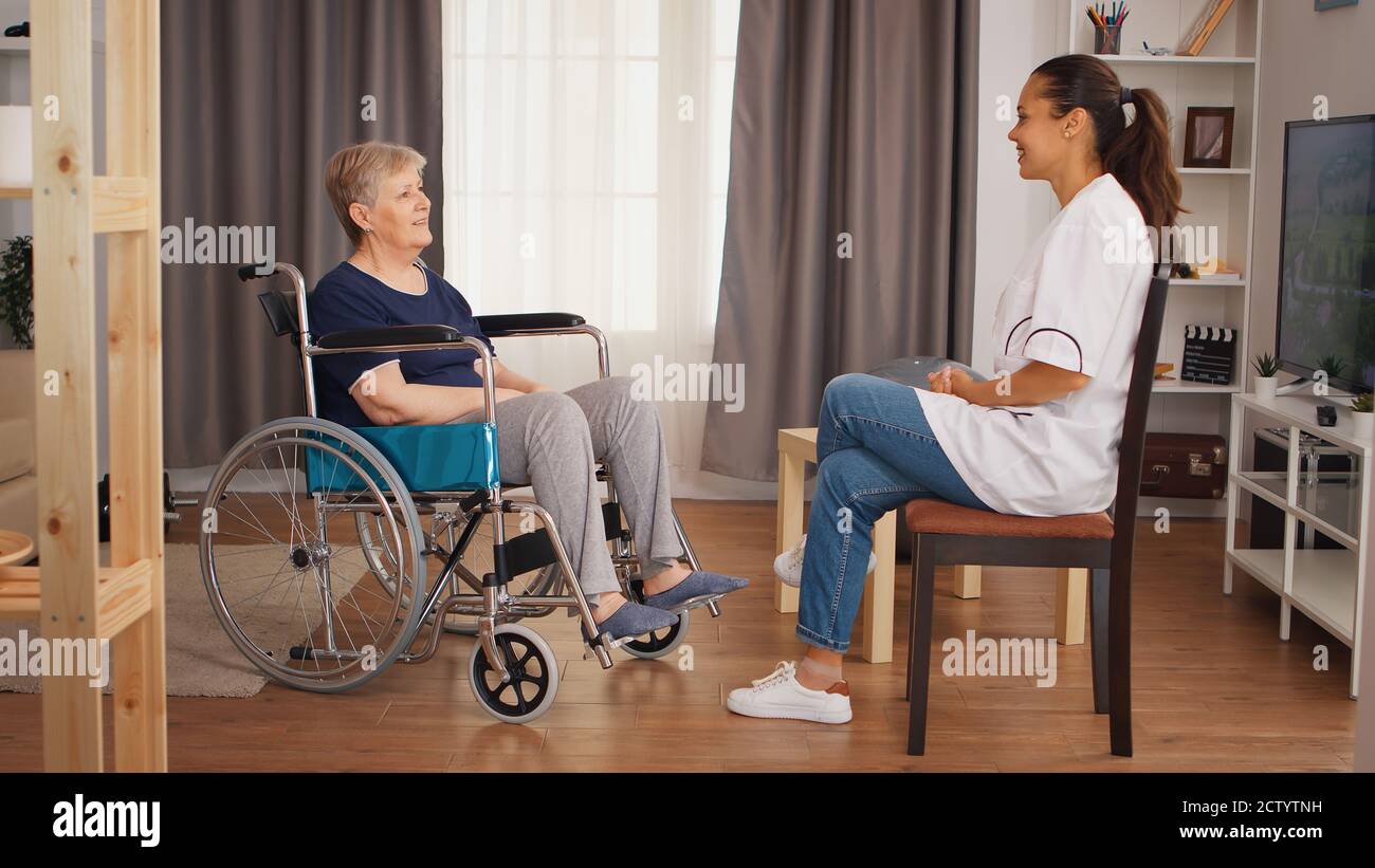 Donna anziana in sedia a rotelle che ha una conversazione con l'infermiere. Casa di riposo per anziani, assistenza sanitaria, assistenza sanitaria, assistenza sociale, medico e assistenza domiciliare Foto Stock