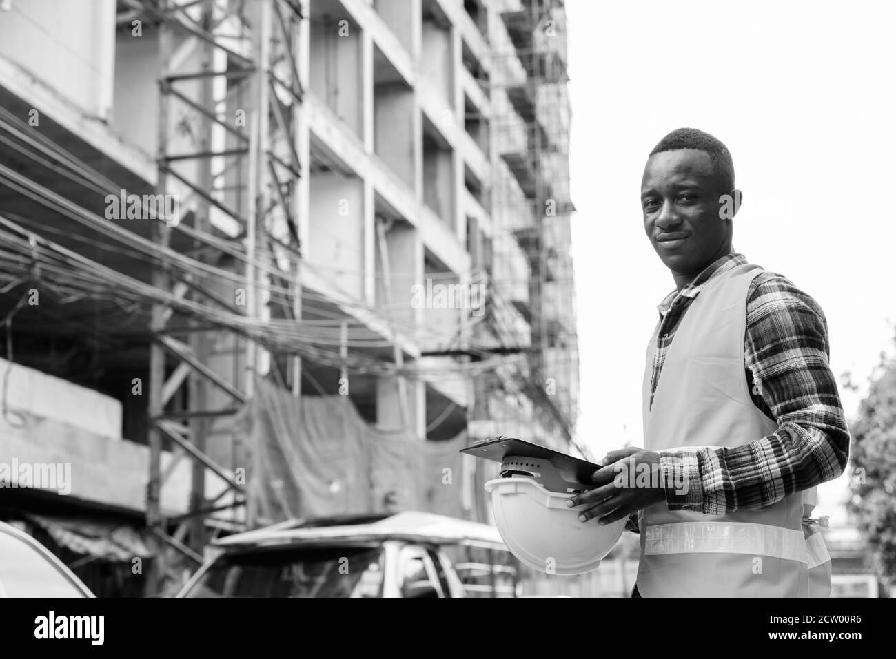 Giovane Africano nero uomo lavoratore edile azienda negli appunti e elmetto in cantiere Foto Stock