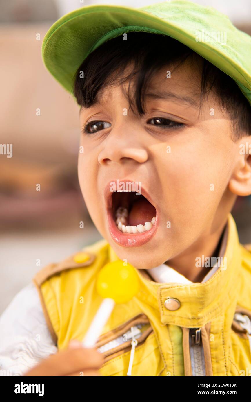 Taglia il ragazzino che mangia caramelle lollipop e si diverte all'aperto di giorno in giorno. Foto Stock