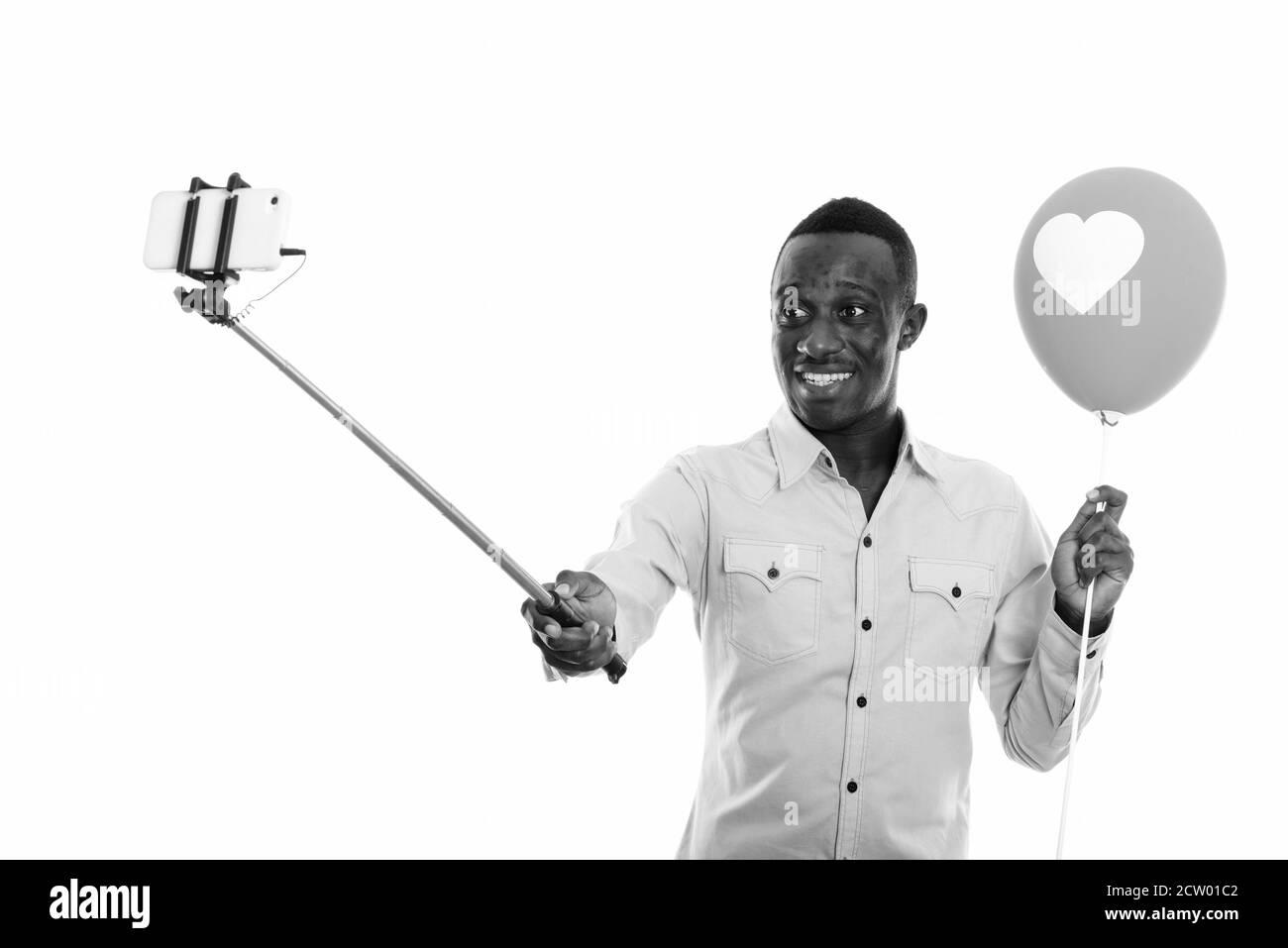 Studio shot di giovane felice africano uomo che tiene in baleno con segnale cardiaco durante la presa del selfie con il telefono sulla levetta del selfie Foto Stock