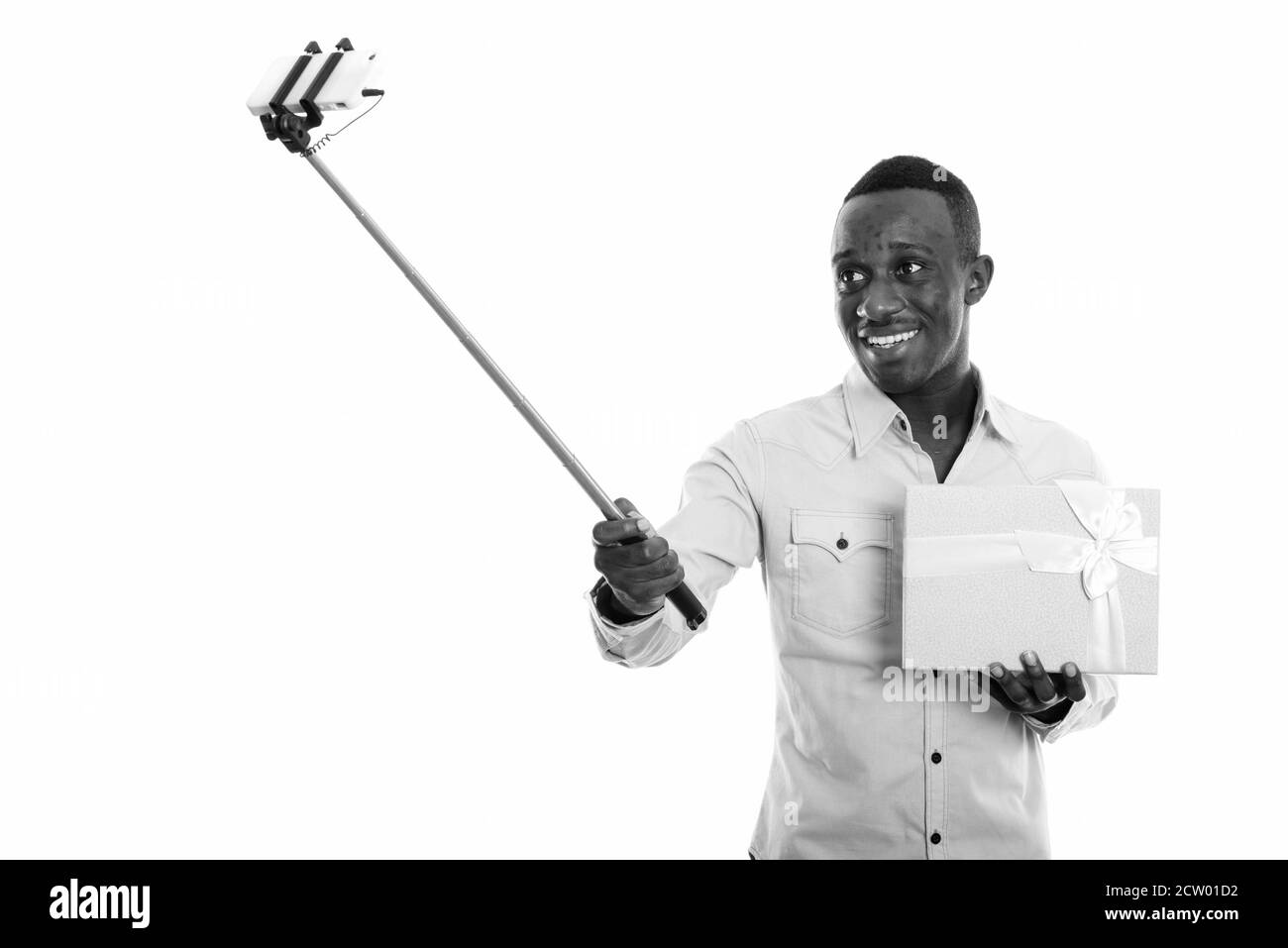Felice giovane africano uomo che tiene scatola regalo mentre prende selfie con il telefono cellulare su una chiavetta per selfie Foto Stock