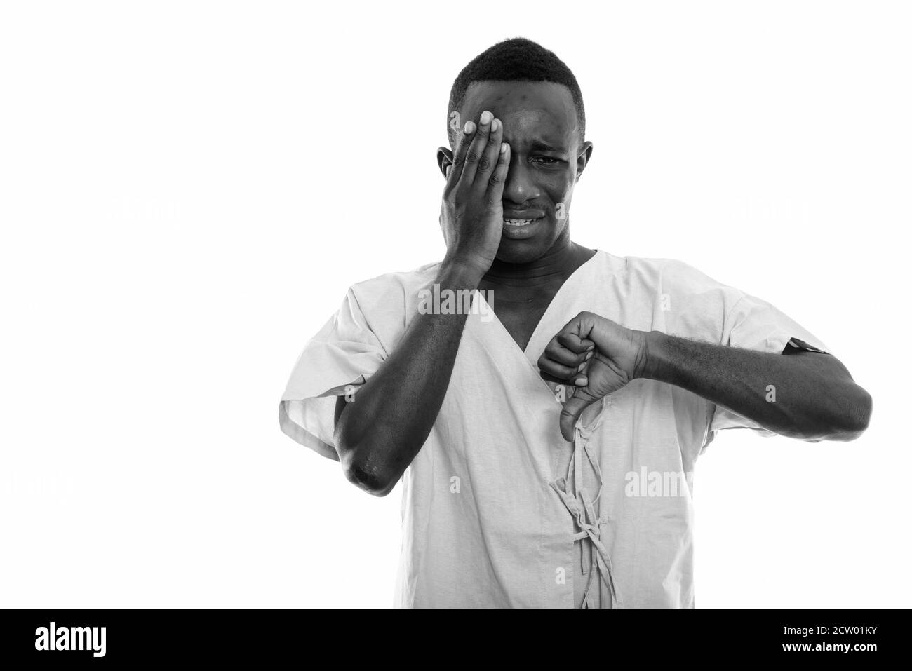 Studio shot del giovane africano nero uomo paziente cercando triste mentre ricopre la faccia e dando il pollice verso il basso Foto Stock