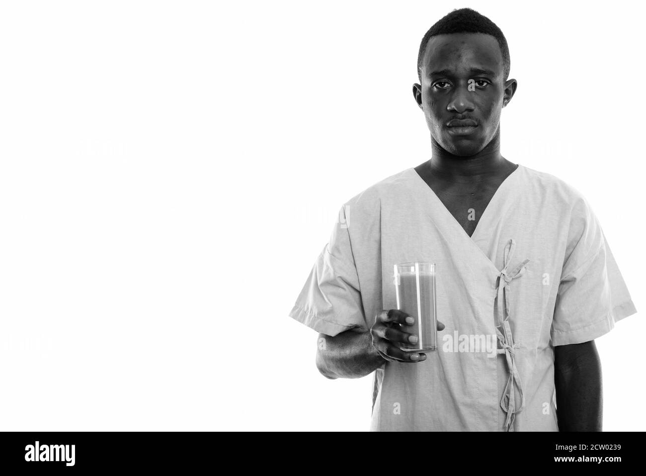 Studio shot di giovane uomo africano nero paziente tenendo vetro di frullato vegetale Foto Stock