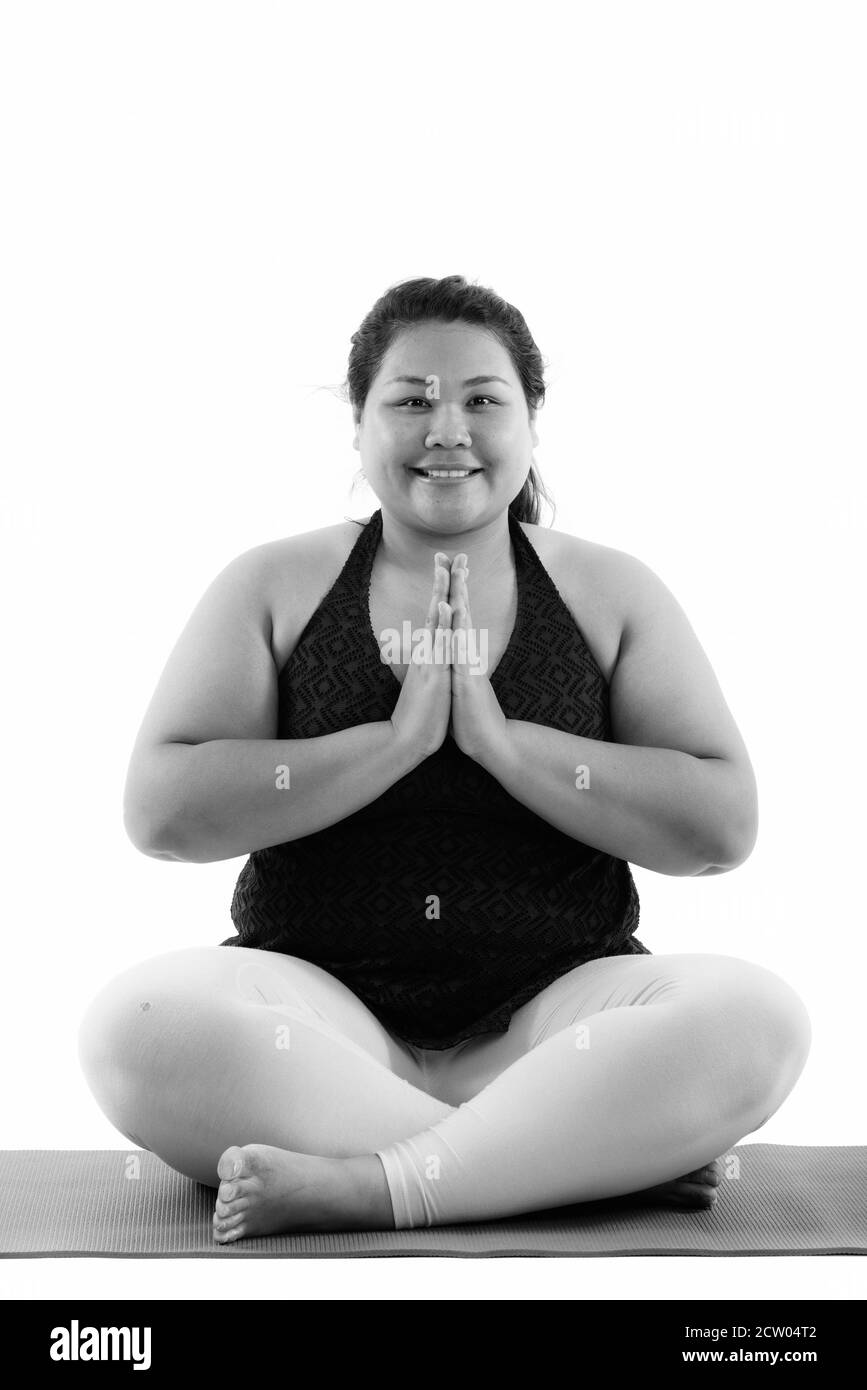 Studio shot di giovani felici fat donna asiatica sorridente e seduta meditando con entrambe le mani Foto Stock