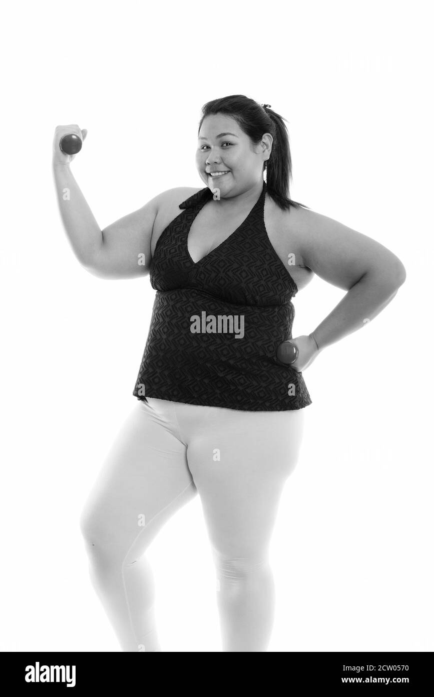 Studio shot di giovani felici fat Asian donna sorridente e in piedi durante l'esercizio con manubri Foto Stock