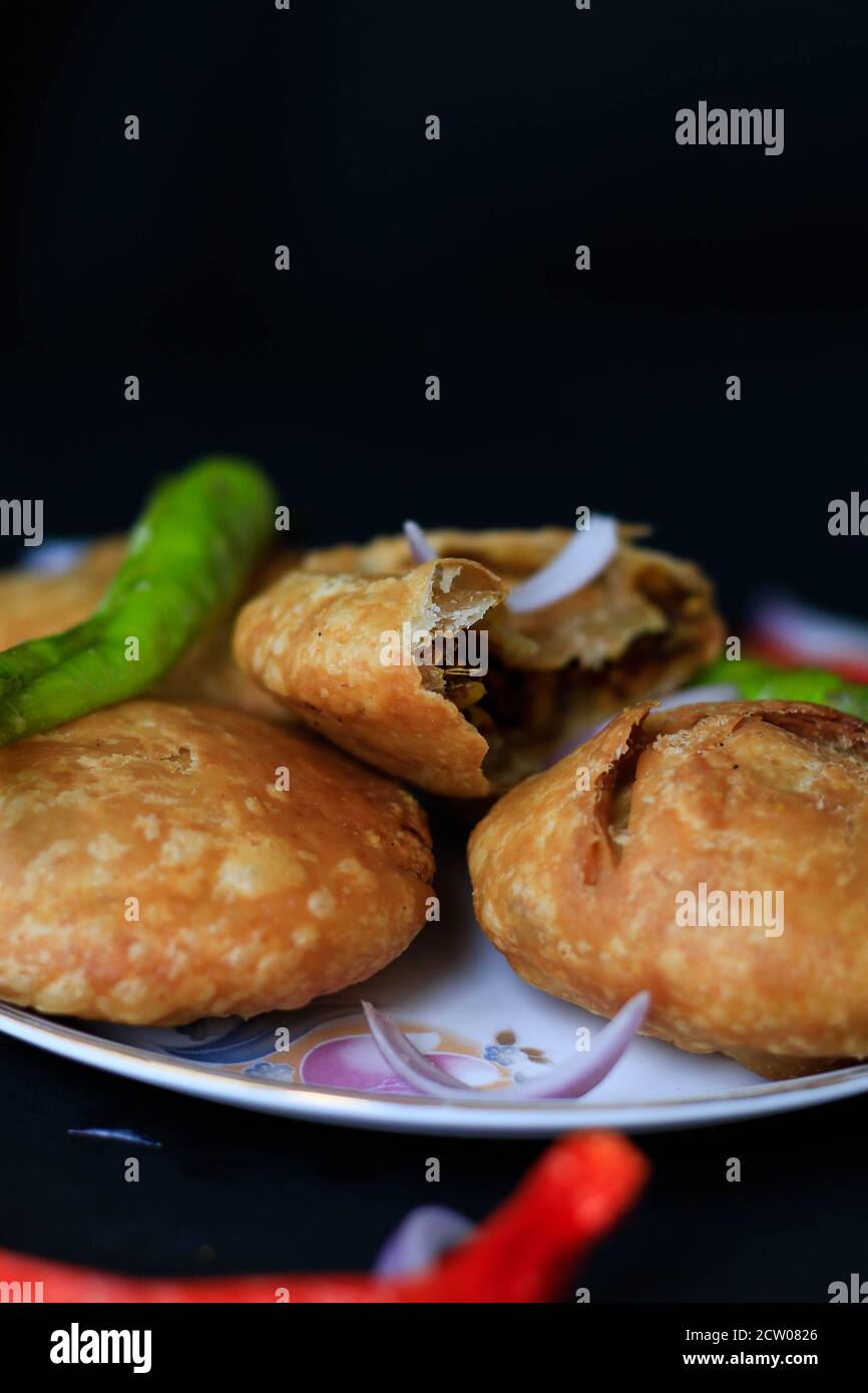Gustoso snack indiano kachori servito con peperoncini verdi e cipolle con una bella sfocatura e uno sfondo nero. Foto Stock