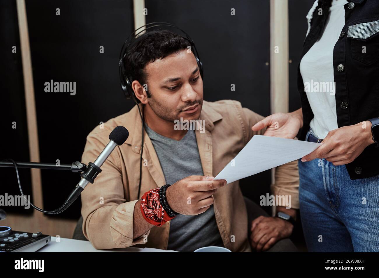 Ritratto di un giovane ospite di radio maschile che guarda serio mentre riceve, tenendo un copione, preparandosi per moderare uno spettacolo dal vivo in studio Foto Stock