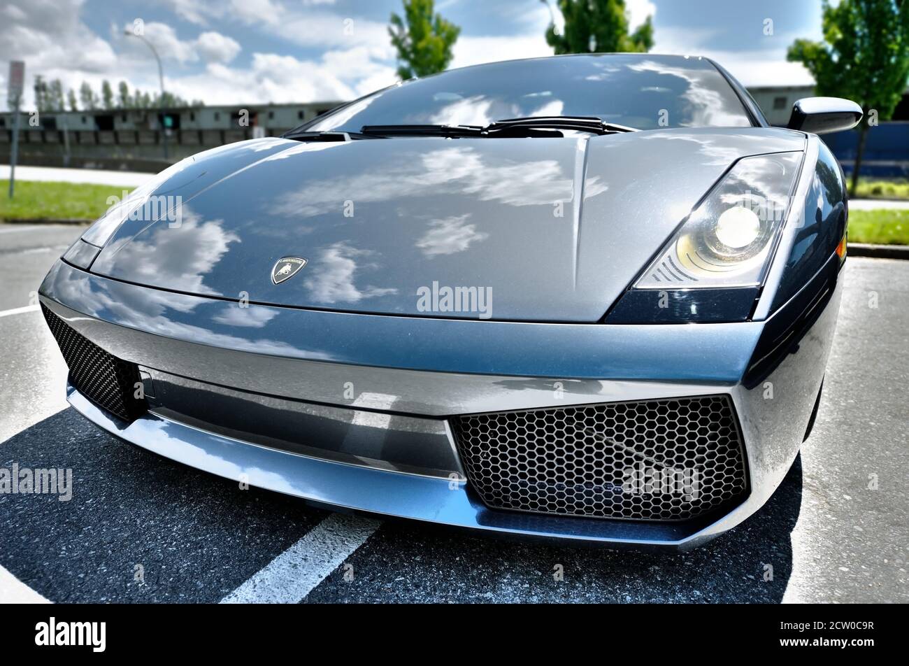 Vista frontale grandangolare del potente Lamborghini Aventador Roadster di colore blu parcheggiato su una strada pubblica. Il cielo e le nuvole si riflettono sul metallo lucido. Foto Stock