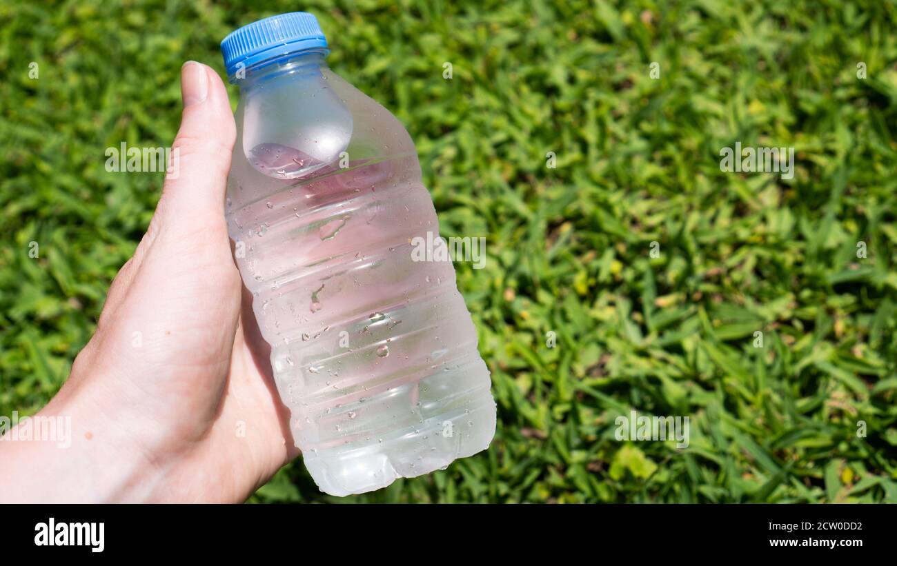 Tenere a mano una bottiglia di plastica blu di acqua ferma sull'erba verde. Rinfresco estivo. Bere molta acqua Foto Stock