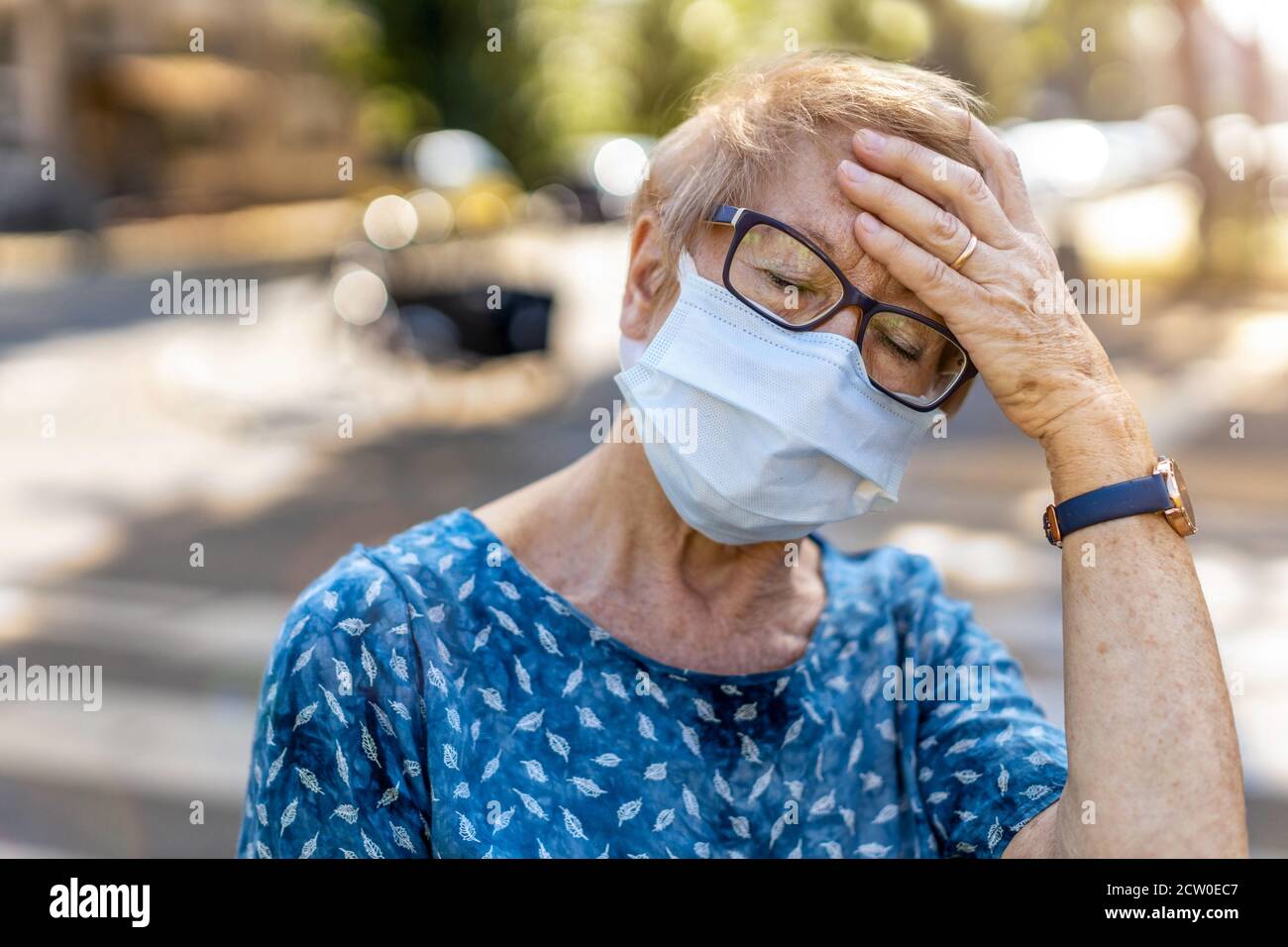 Donna anziana con maschera protettiva che soffre di mal di testa Foto Stock