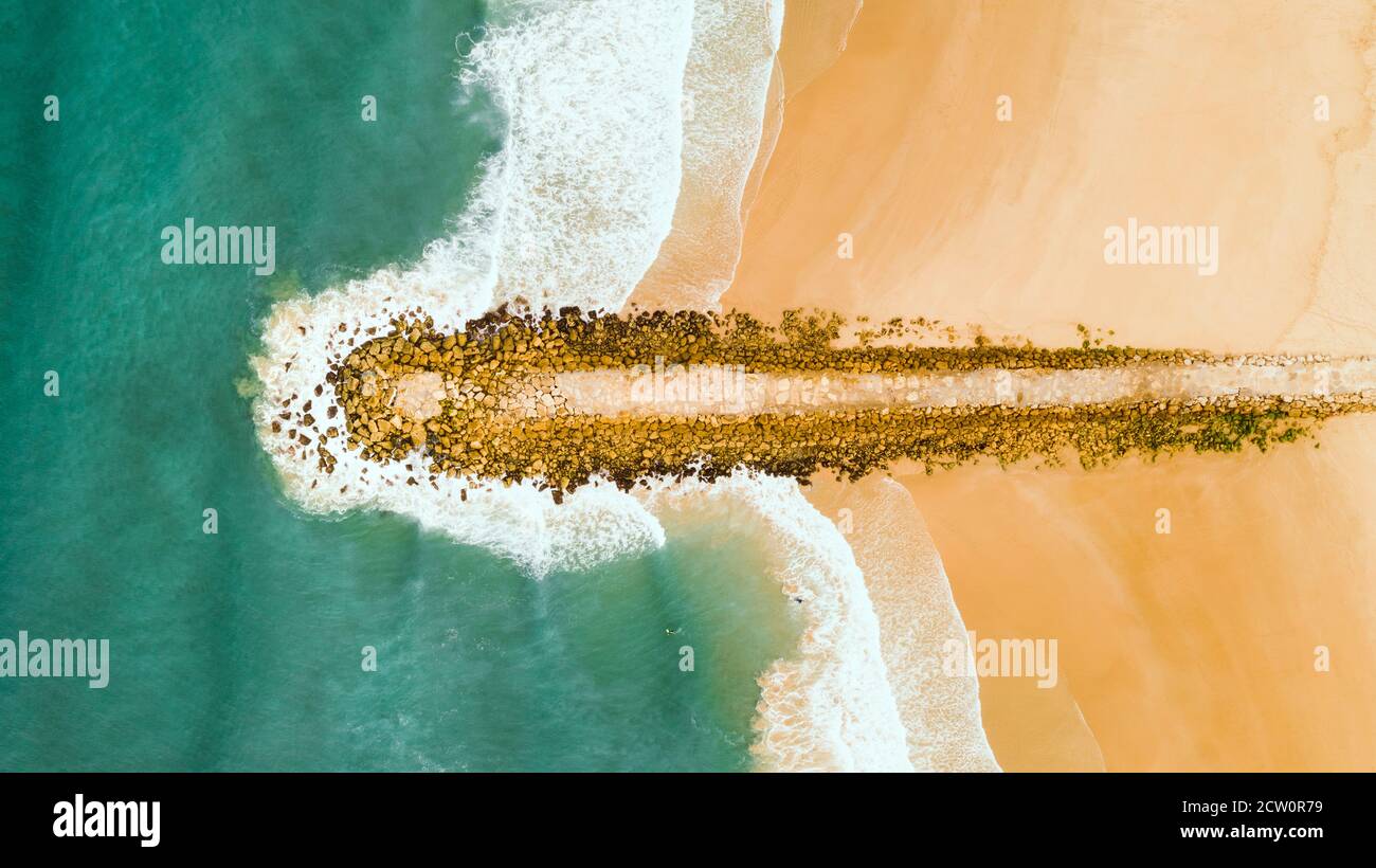 Molo in pietra o acqua frangiflutti sulla spiaggia di sabbia. Calmo oceano verde. Foto drone Foto Stock