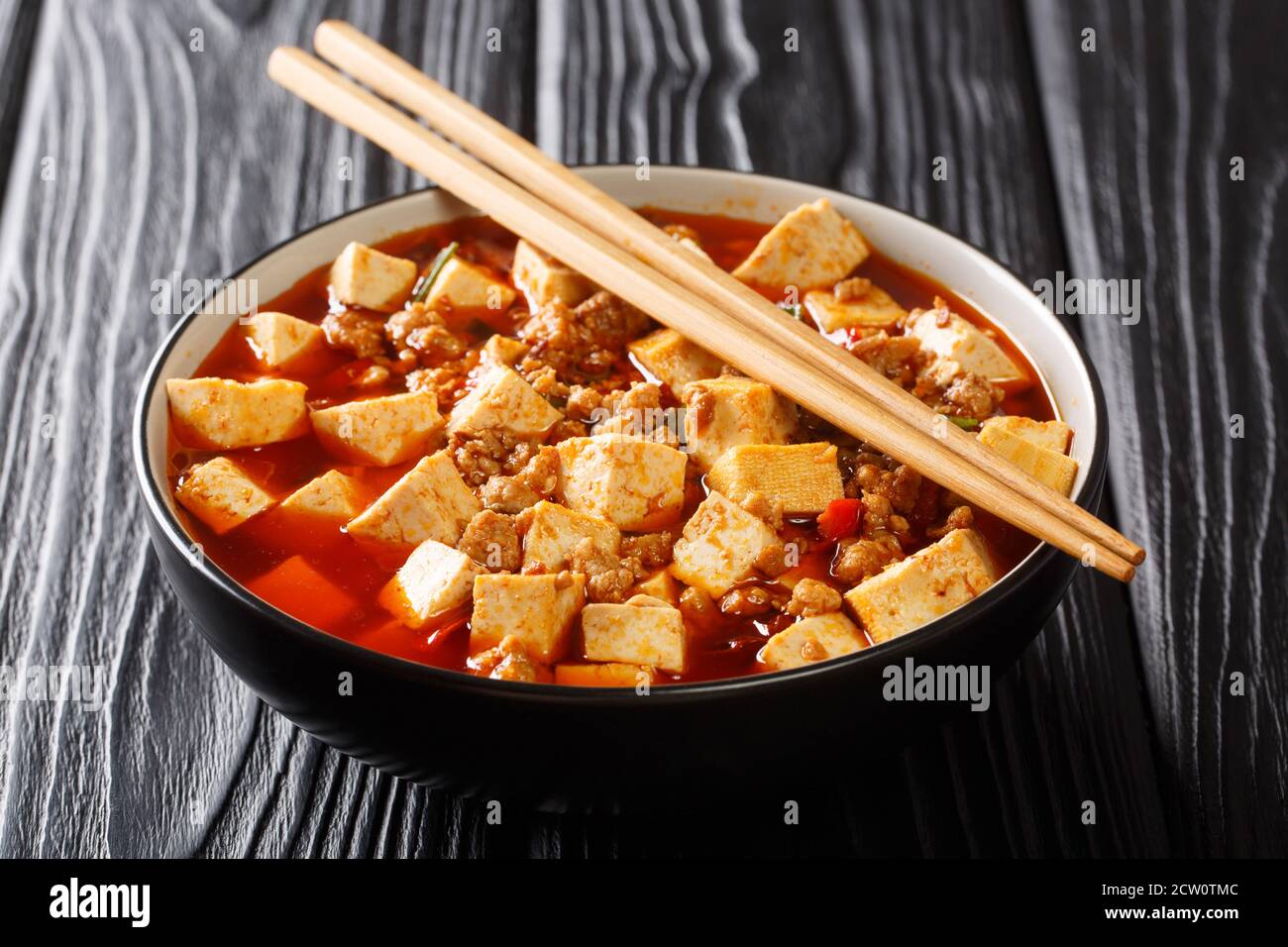 Il tofu cinese del mapo è maiale e tofu fritti in un primo piano di salsa calda in una ciotola sul tavolo. Orizzontale Foto Stock