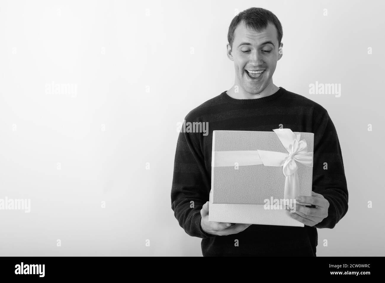 Studio shot di giovani felici muscolare di uomo sorridente durante l'apertura della confezione regalo contro uno sfondo bianco Foto Stock