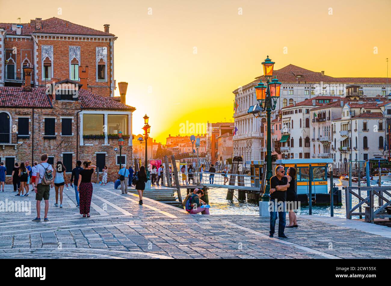 Venezia, Italia, 13 settembre 2019: Persone turisti a piedi lungo Fondamenta Salute Embankment Promenade vicino al molo del Canal Grande al tramonto, Regione Veneto, Italia settentrionale. Vista contro il sole Foto Stock