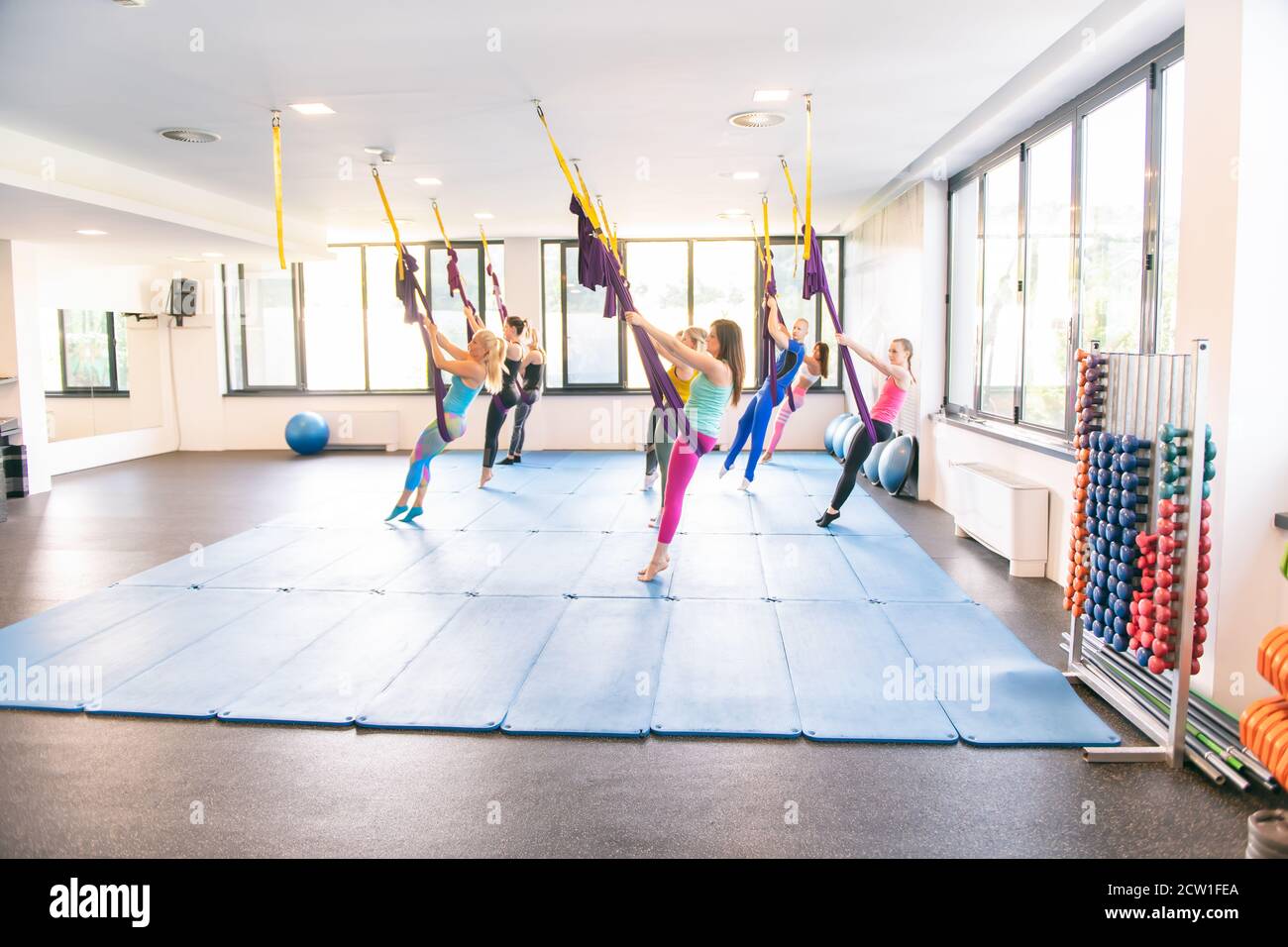 Gruppo di giovani donne e un uomo muscolare che fa esercizi di yoga antigravitazionale. Fitness Fly. Amaca viola Foto Stock