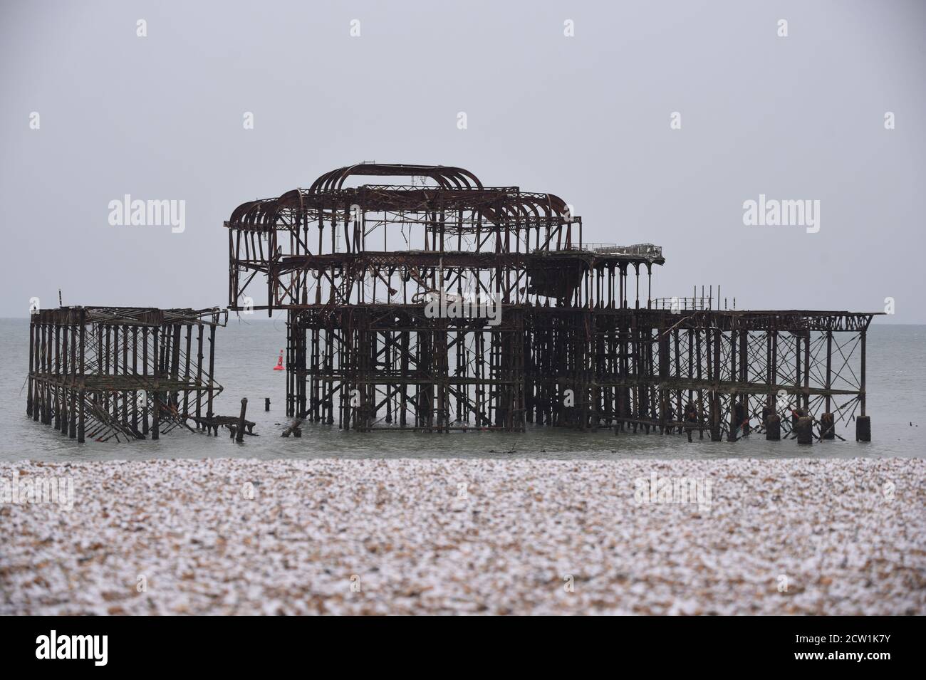 Una mattina fredda sulla spiaggia di Brighton, con neve sui ciottoli e le rovine del vecchio molo sullo sfondo. Foto Stock