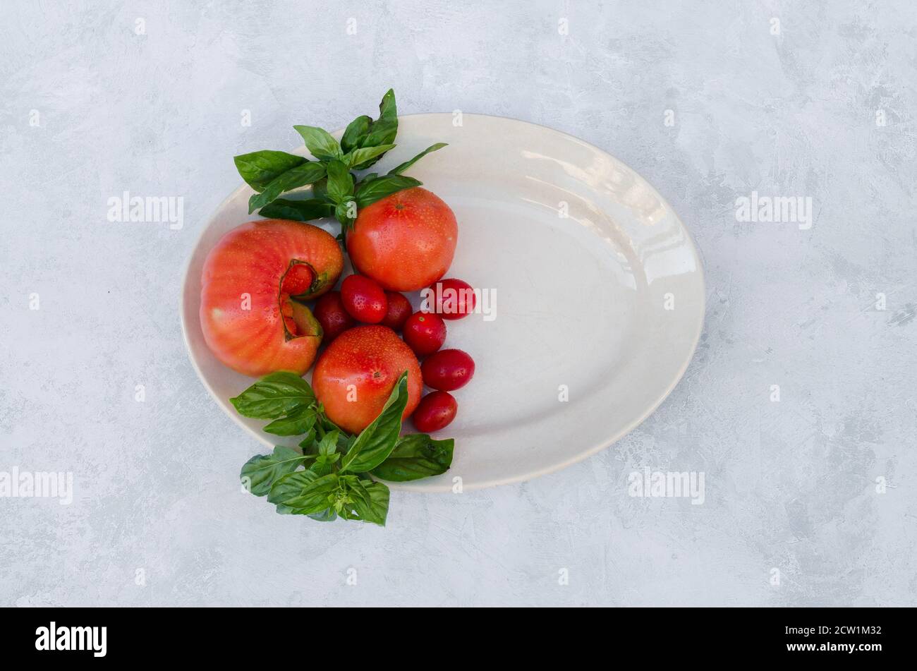 pomodori freschi con foglie verdi su un vassoio bianco Foto Stock