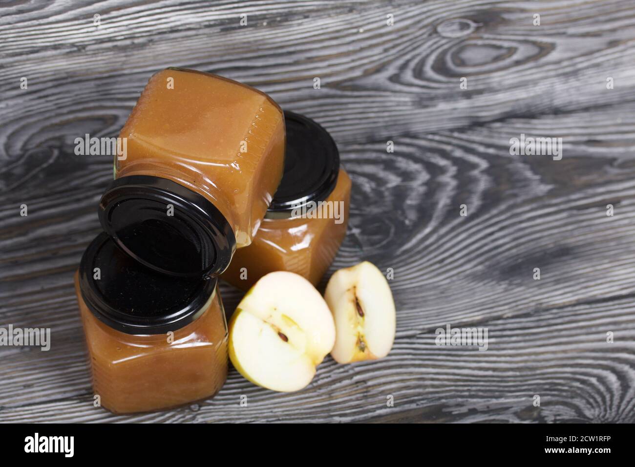 Marmellata di mele in vasi. Nelle vicinanze si trovano le fette di mela. Su tavole spazzolate, verniciate in bianco e nero. Foto Stock