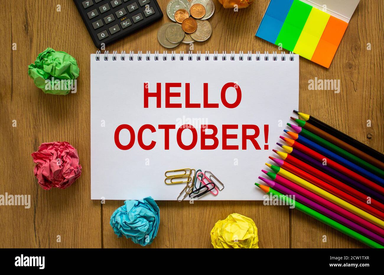Nota bianca con iscrizione 'ciao october' su bel tavolo di legno, carta colorata, matite colorate, graffette, monete e calcolatrice. Business con Foto Stock