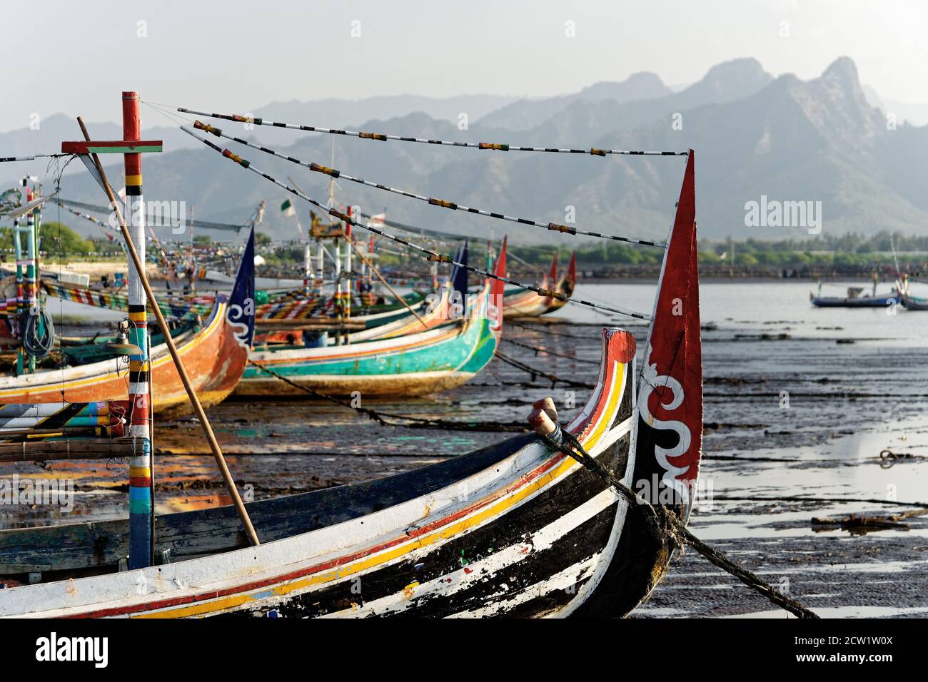 Le tipiche barche da pesca colorate si trovano sulla spiaggia a bassa marea, sullo sfondo una catena montuosa nella foschia - Ubicazione: Indonesia, Isola di Giava, Panar Foto Stock