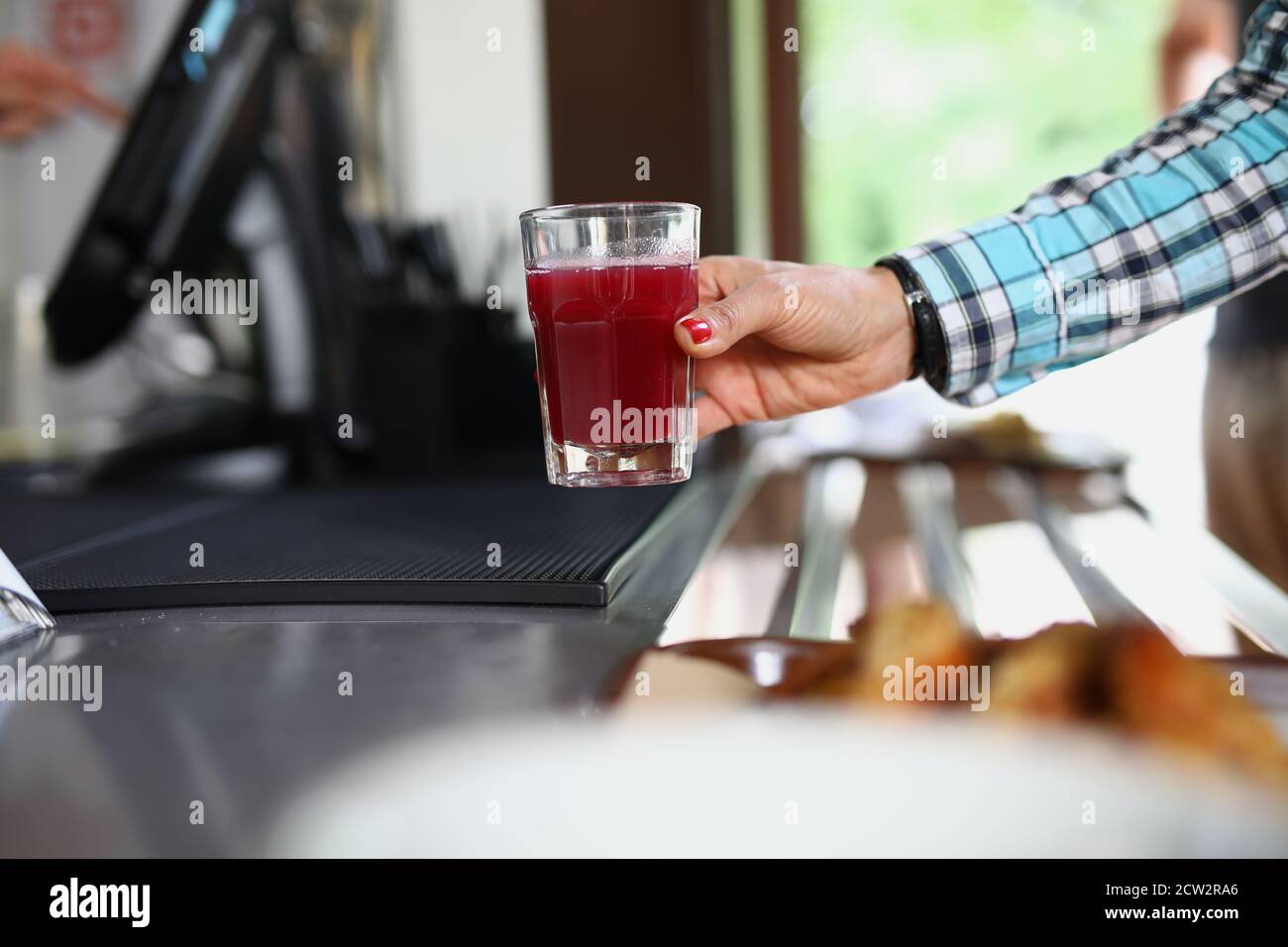 La mano della donna tiene il vetro nel caffè con liquido rosso simile alla frutta o alla gelatina Foto Stock