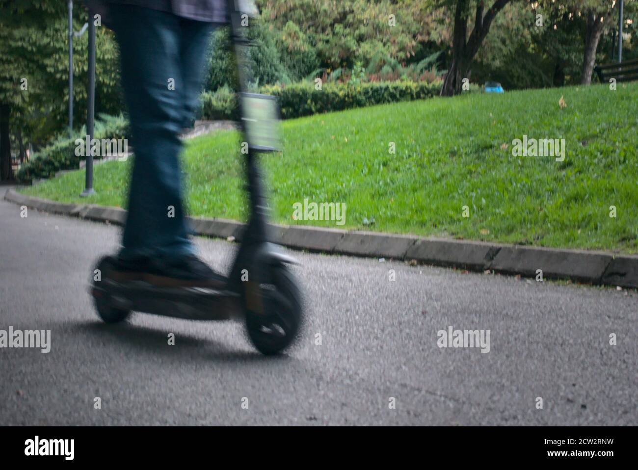 Uomo che guida scooter elettrici eco-friendly alla moda nel parco verde in una soleggiata giornata autunnale primo piano a bassa angolazione Foto Stock