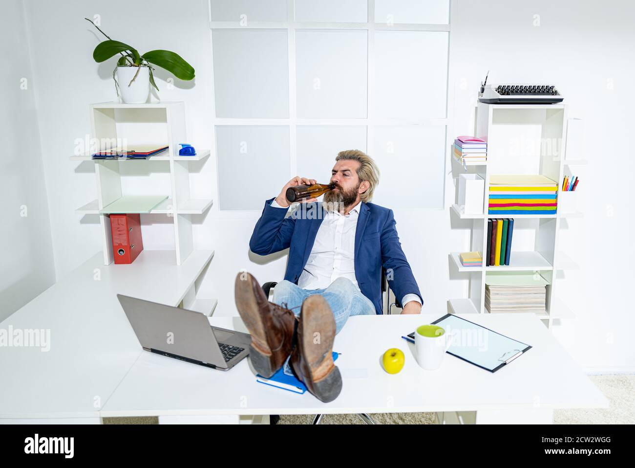 Un uomo d'affari ubriaco annoiato in ufficio alla fine della giornata lavorativa. Uomo d'affari ubriaco con una bottiglia di alcol. Lavoratore ubriaco in ufficio, trasportando casualmente una bottiglia Foto Stock