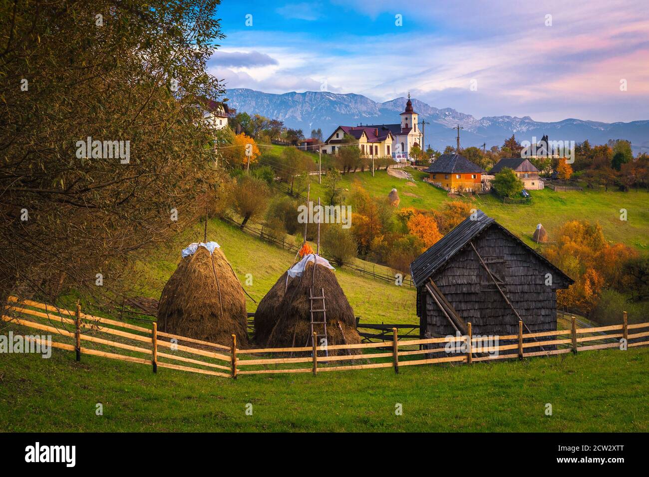 Splendido paesaggio di campagna autunnale e colorati alberi decidui sulle colline. Pagliai e capanna in legno nel giardino al tramonto, Carpazi, Trans Foto Stock