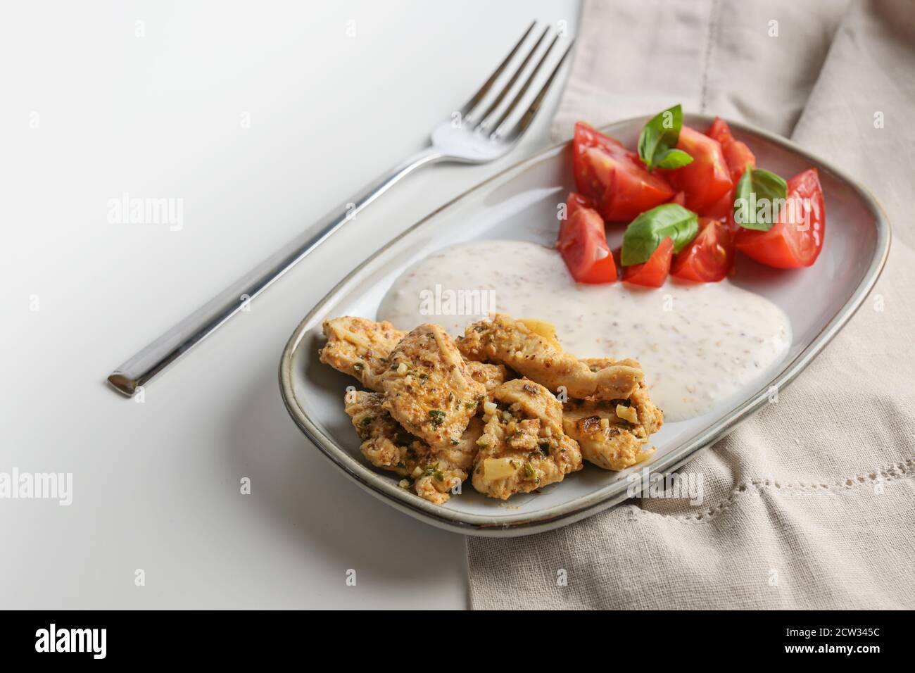 Pollo marinato orientale con salsa al sesamo allo yogurt e pomodori con guarnitura al basilico su un piatto e un tavolo grigio brillante, spazio copia, fuoco selezionato, n Foto Stock