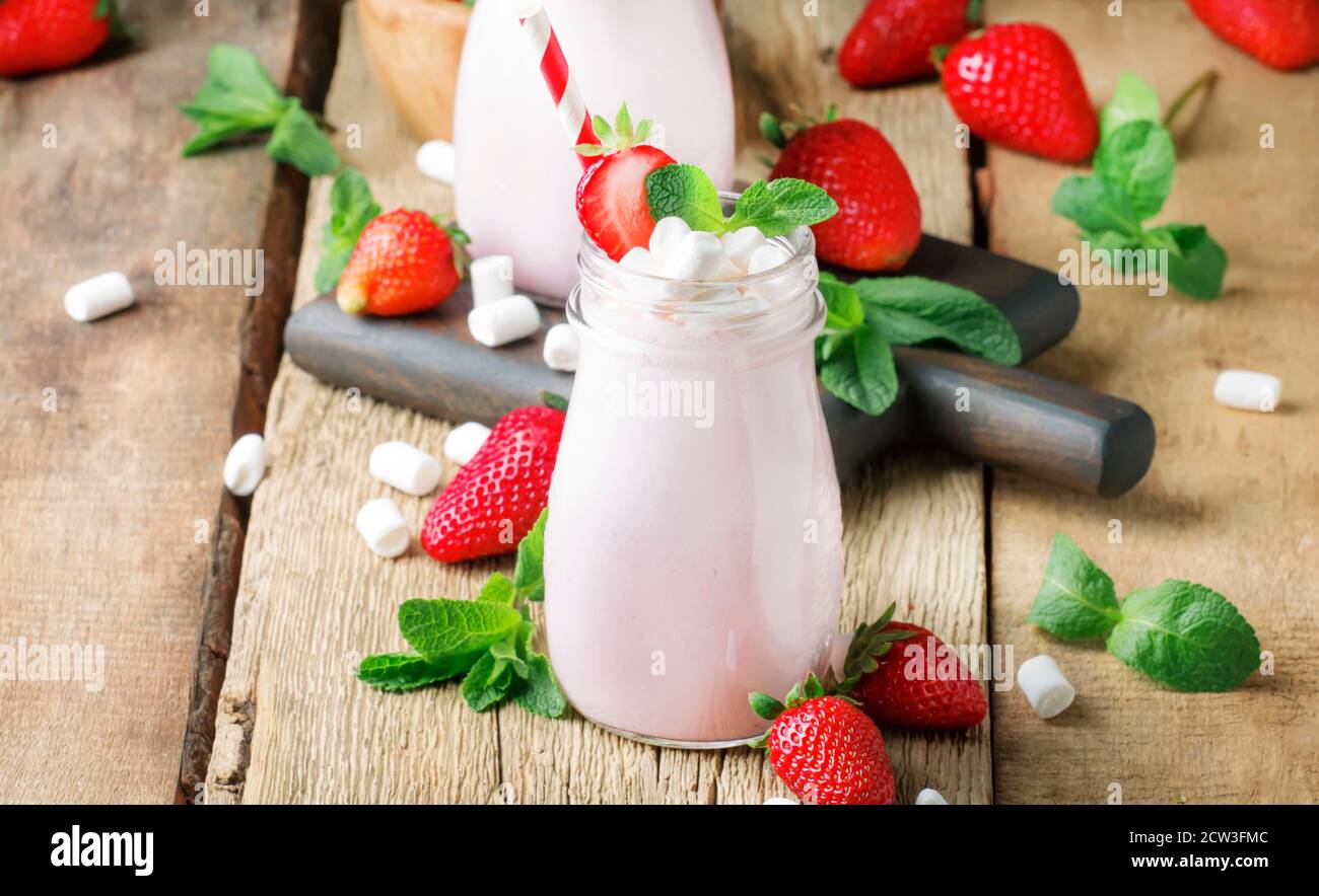 Frullati di fragole e cocktail con frutti di bosco freschi e menta verde, marshmallows decorati, bevanda estiva, legno vecchio sfondo, fuoco selettivo Foto Stock