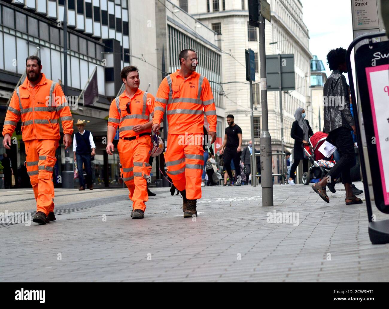 Tre lavoratori in uniformi arancioni riflettenti su Corporation Street, Birmingham Foto Stock