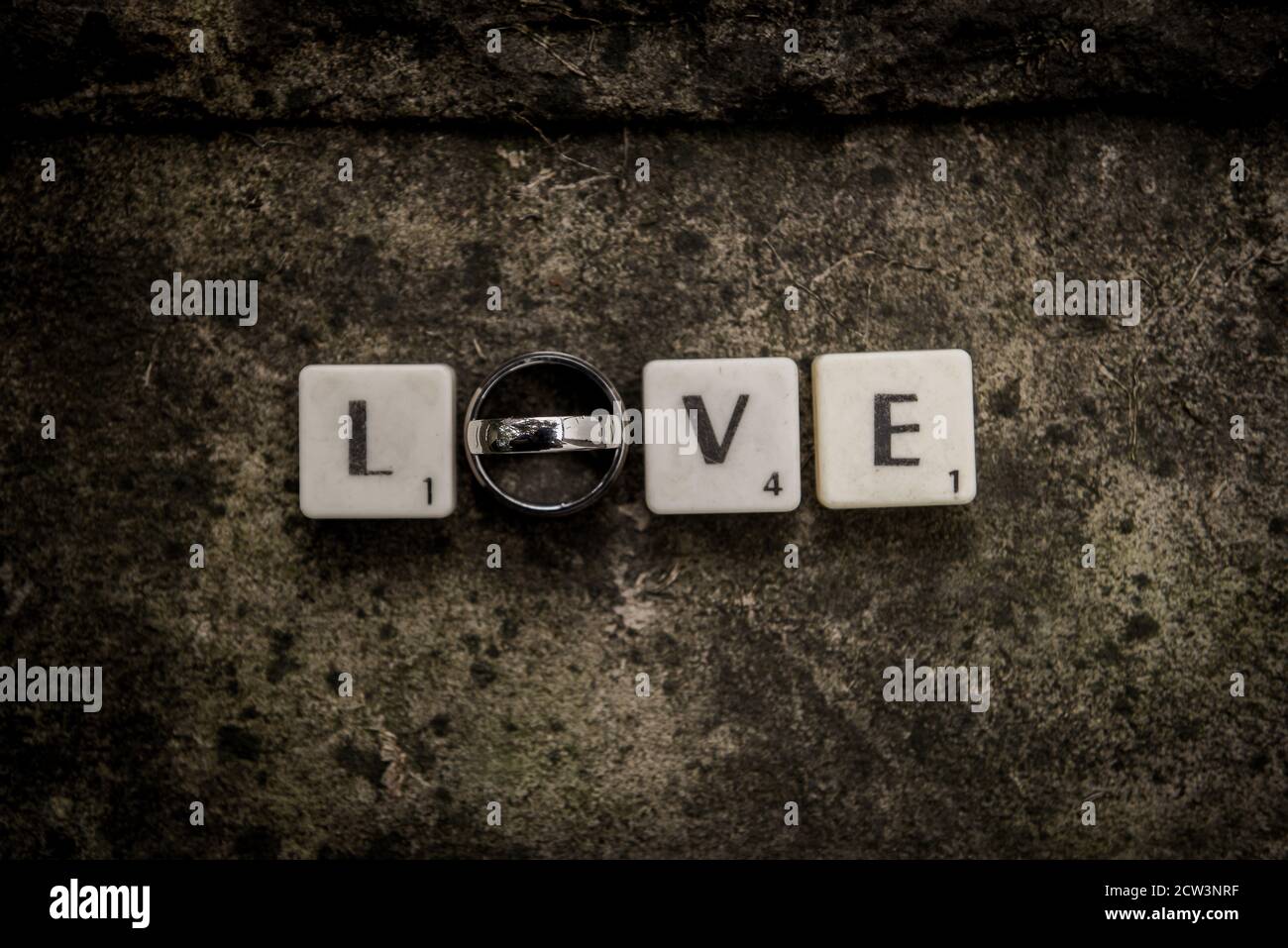 Piastrelle con lettere che ortografia Amore con gli anelli di nozze in un diritto linea su fondo di pietra Foto Stock