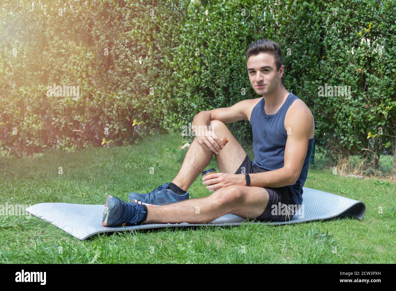 giovane atleta di fitness seduto sul tappetino e di riposo avere un piccolo caffè e un bar energetico dove rilassarsi recuperare in una giornata di sole Foto Stock