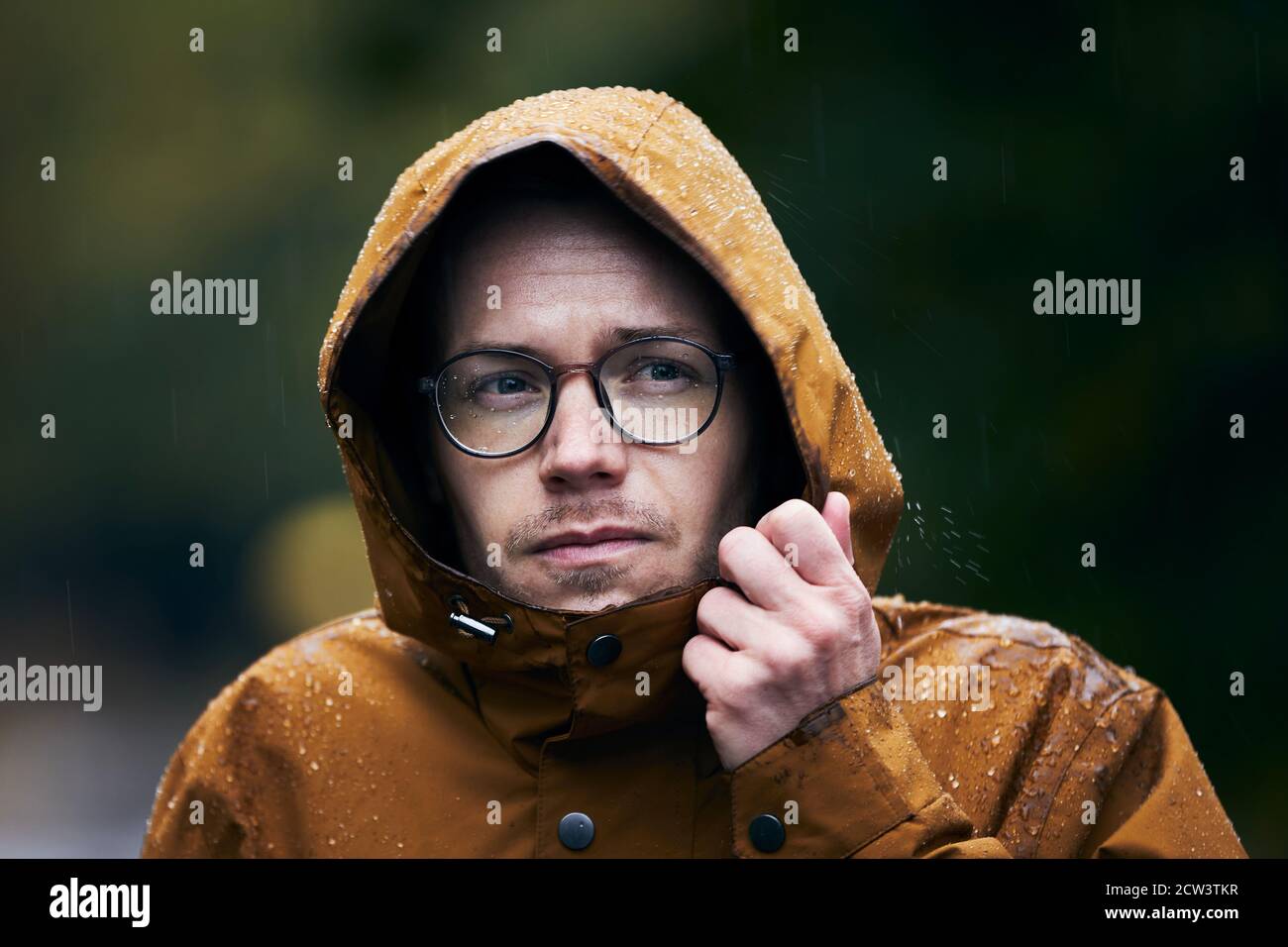 Pioggia intensa durante il giorno d'autunno. Ritratto di giovane uomo in giacca impermeabile. Foto Stock