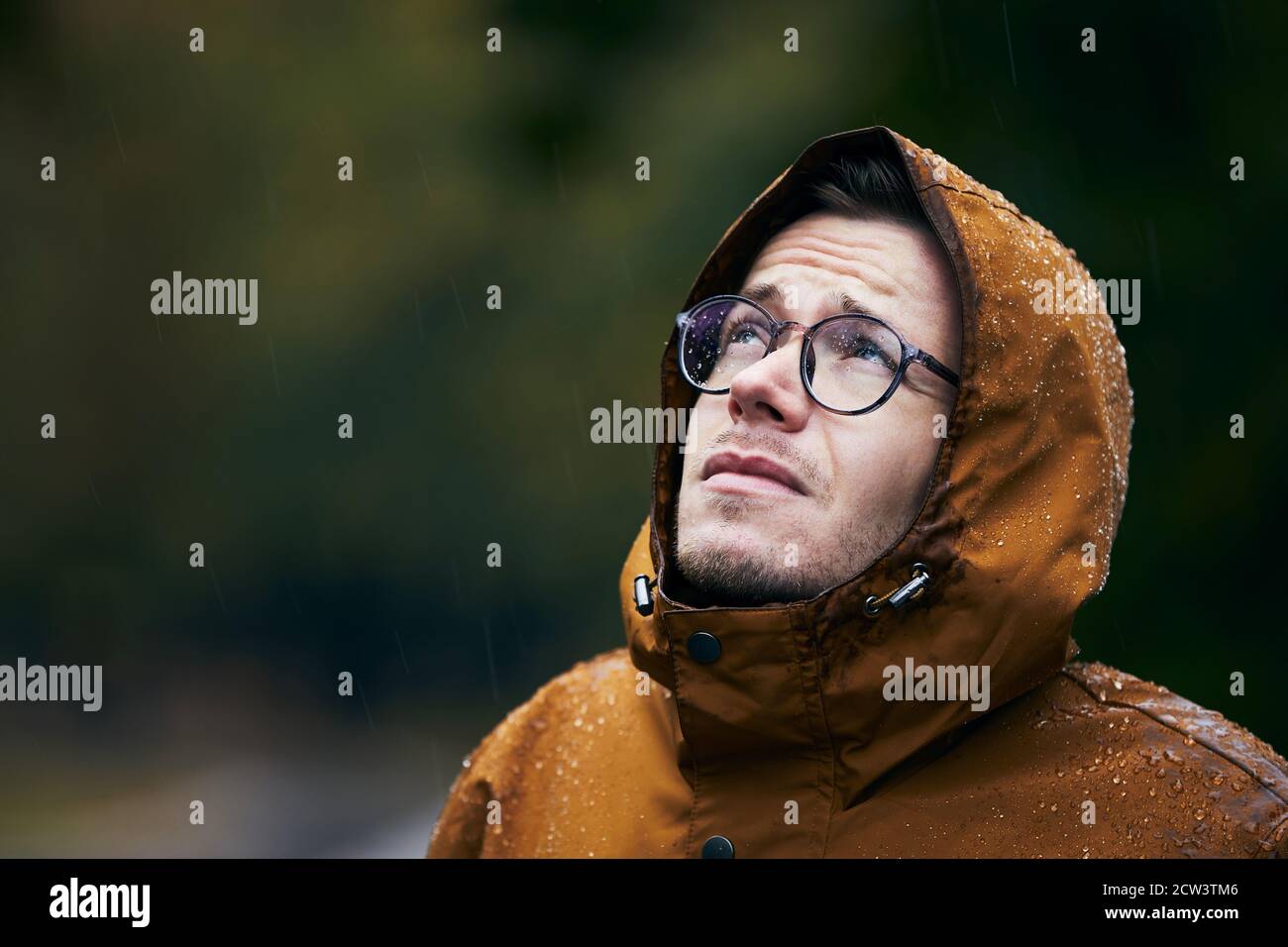 Pioggia intensa durante il giorno d'autunno. Ritratto di giovane uomo in giacca impermeabile. Foto Stock
